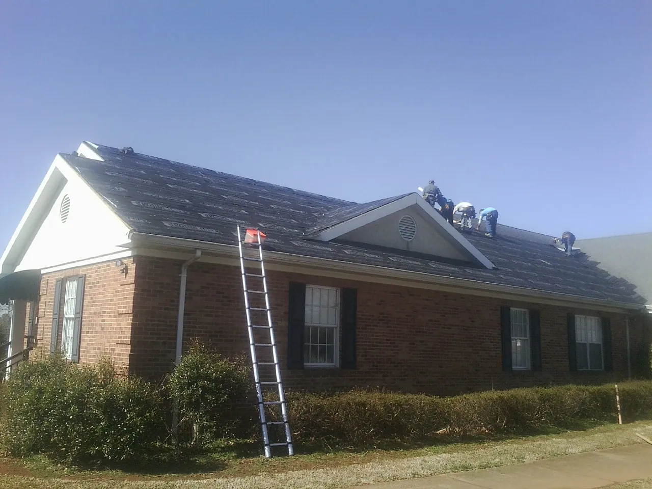 Crew tearing shingles off a brick ranch roof with a ladder set — Metal Roof Repair work by our crew in Creighton