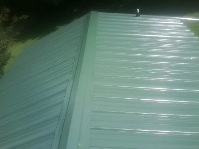 New green metal panels meeting at the ridge of a roof — Flat Roof Repair work by our crew in Creighton