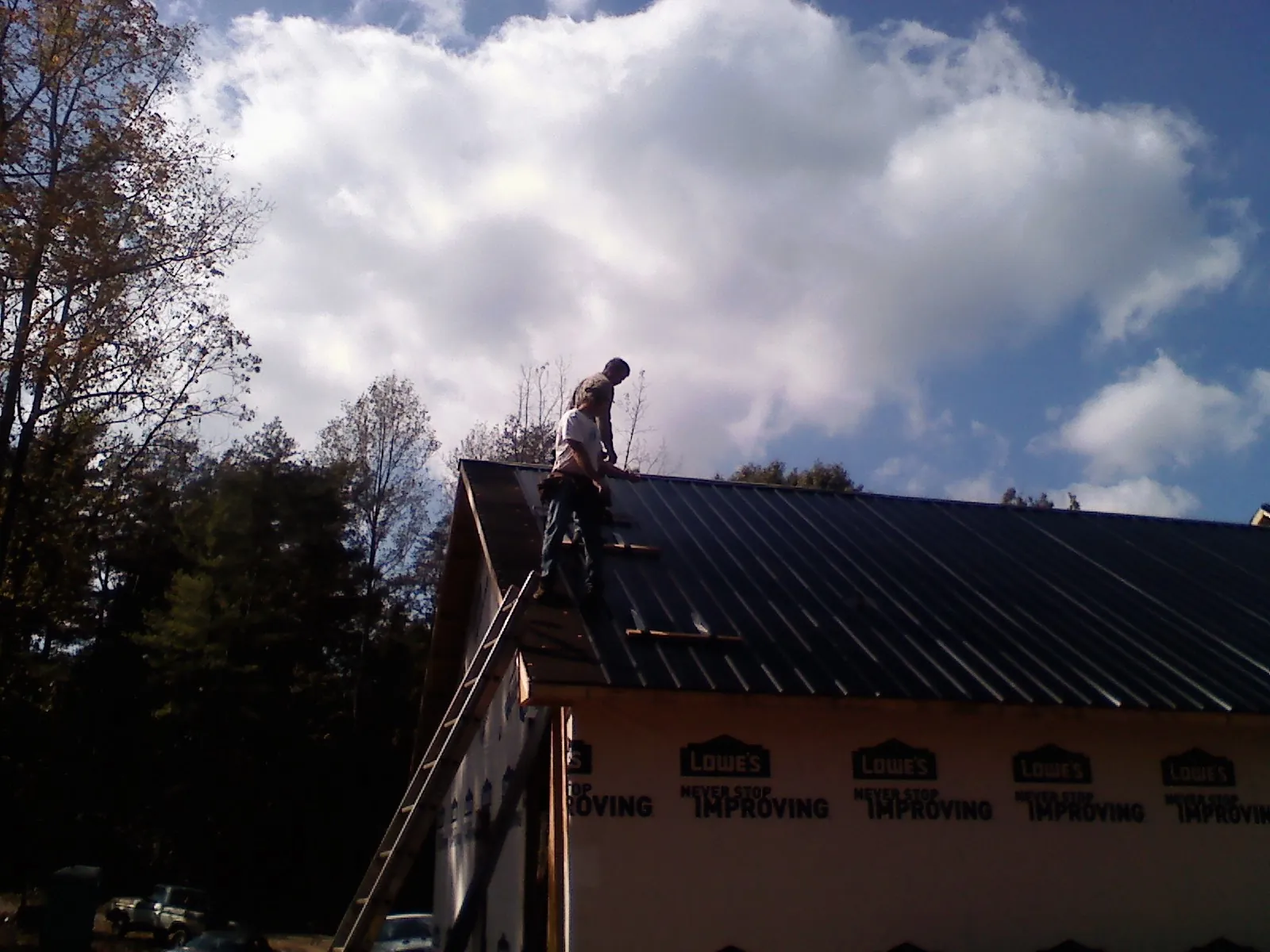 Roofer fastening dark metal panels high against a cloudy sky, from a Roof Inspection job in Creighton